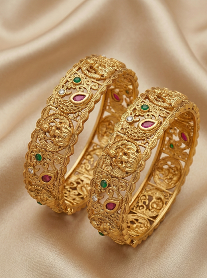Pair of gold bangles with gemstones on a beige fabric background