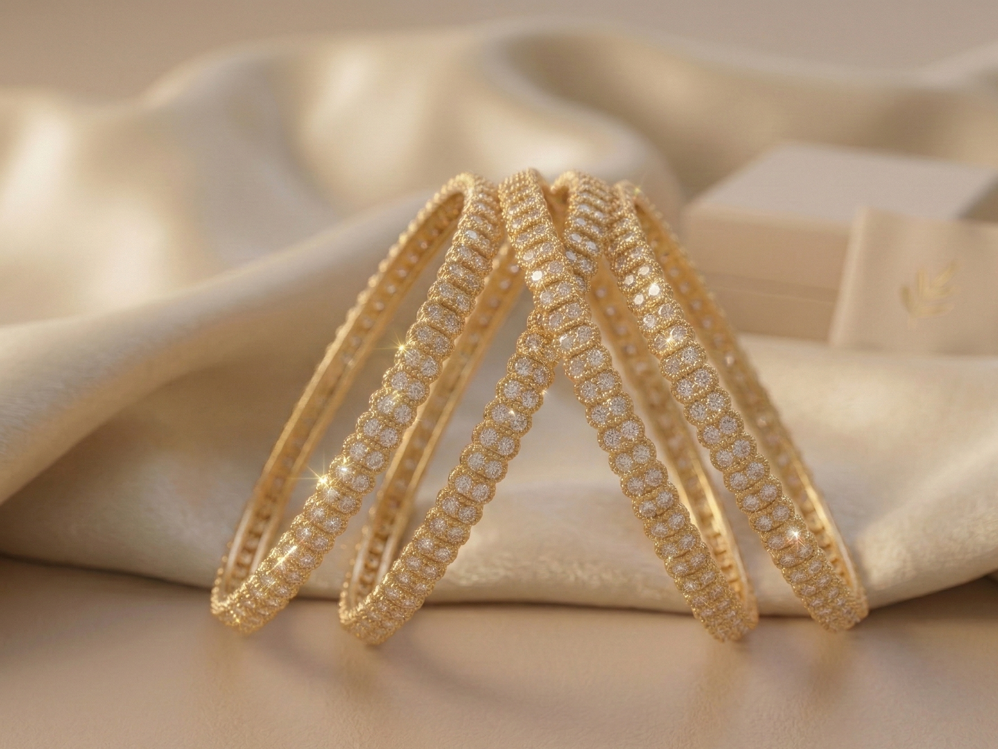 Three gold bangles with intricate designs on a soft beige fabric background