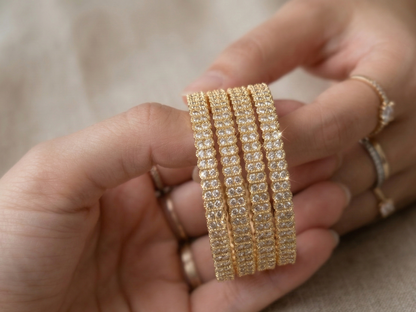 Gold bracelet with clear stones held in a hand against a neutral background
