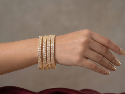 Hand wearing multiple gold bracelets on a neutral background