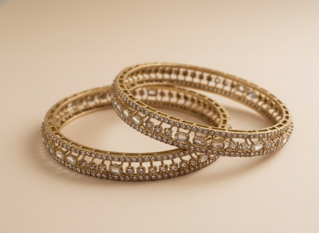 Pair of gold bangles with gemstone accents on a beige background